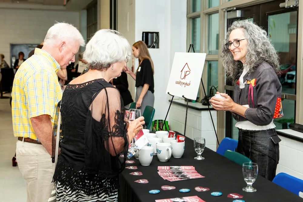A woman stands behind a table talking to two people