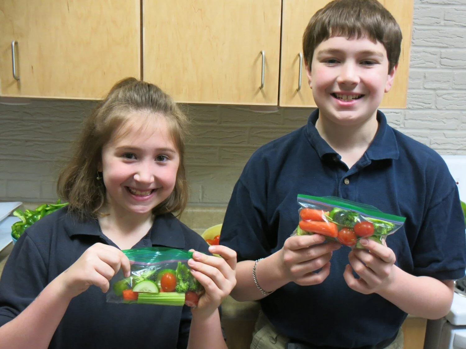 two smiling children showing off their vegetable snacks